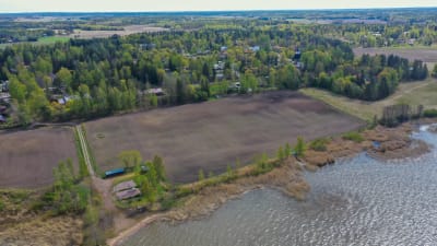 En flygbild på åkrar, skog och bebyggelse vid en strand.