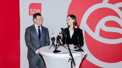 Antton Rönnholm och Sanna Marin står vid ett vitt bord med mikrofoner och väntar på resultatet av förhandsrösterna.