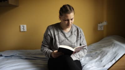 Nainen istuu sängyllä ja lukee kirjaa.