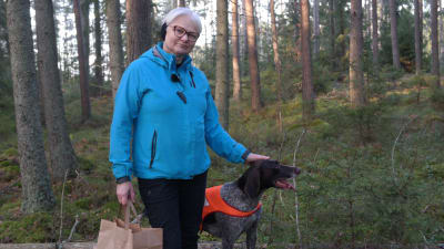 Eija Lamsijärvi med en hund i skogen.