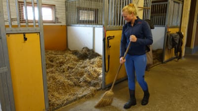 Patricia Westman sopar stallgolvet utanför hästarnas boxar.