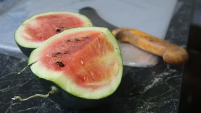 En liten uppskuren vattenmelon på ett bord, en kniv i bakgrunden.