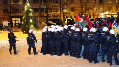 Ett stort antal kravallpoliser pressar en grupp demonstranter från Tölö torg i Helsingfors. En julgran står tänd på det snöklädda torget.