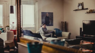 Carolina Sinisalo sitter i soffan och på väggen ovanför henne finns en stor bild av sonen Robin.