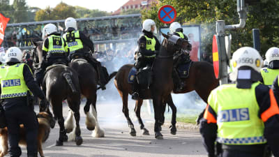 Poliser på polishästar rider på Göteborgs gator under en stor demonstration. Rök av en rökbomb syns på vilden. 