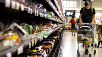 Man med shoppingvagn kollar utbudet i matbutik. 