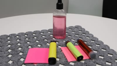 E-cigaretter och en flaska ljusröd smakvätska. E-cigarretterna är avlånga och liknar läppomada eller tändare.