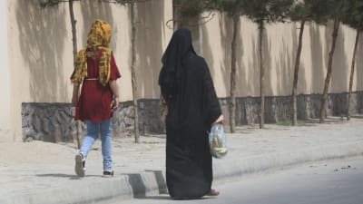 En kvinna i burkha och en ung flicka i huvudduk som går på gatan i Kabul. 
