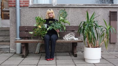 Tia Hassinen sitter på en bänk utanför Strömborgska skolan, med två plantor i handen.