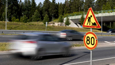 Bilar kör förbi trafikskylt. Skylten visar en hastighetsbegränsning på 80 kilometer per timme.