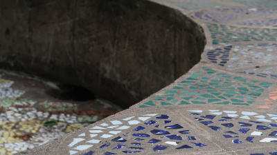 Mosaikmönster i mörkblått, grönt och vitt i en cementfärgad fontän.