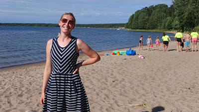 Sofia Stolt står på en sandstrand med simskoledeltagare i bakgrunden.