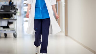 En sjukskötare går i en sjukhuskorridor. Man ser inte huvudet på personen.
