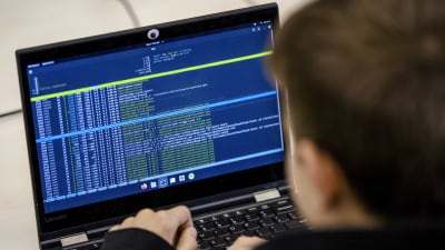 En person fotograferad bakifrån medan han sitter vid en dator och kodar.