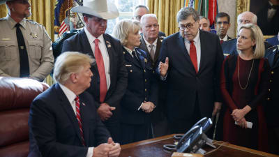 President Trump sittande vid skrivbord, med folk omkring sig, bla jusititieminister Barr och man med stor cowboyhatt.