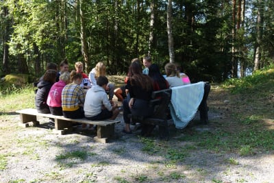 Lägerdeltagare och ledare på Prometheus-lägret i Lojo sitter på bänkar på en gård och diskuterar.