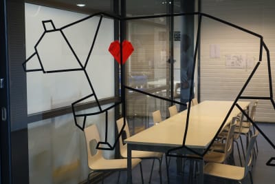 Tomma stolar vid ett långt bord bakom en glasvägg som pryds av en bild på en björn med rött hjärta i Lagstads skola.