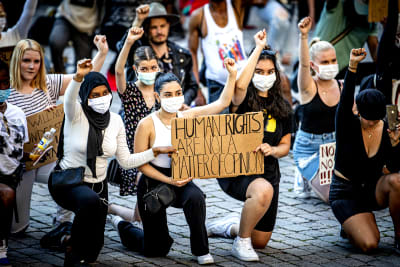 En grupp unga kvinnor knäböjer med en höjd knytnäve. I famnen har de ett plakat med texten Human rights are npt a matter of opinion.