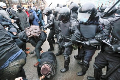 Joukko musta-asuisia mellakkapoliiseja tulee pamppujen kanssa kuvan oikealta laidalta kohti mielenosoittajia vasemmalla. Yksi mielenosoittaja makaa maassa. Yksi poliiseista on nostanut pamppunsa lyödäkseen reppuselkäistä miestä edessään.