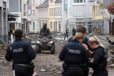 Polis patrullerar i Tyskland under översvämningarna. En person åker fyrhjuling i bakgrunden.