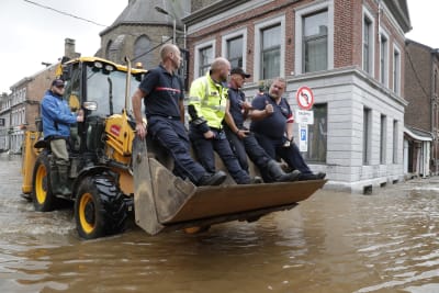 Räddningsinsatsen är i full gång i Belgien. Här åker fyra män i en grävskopa för att komma fram på de vattentäckta vägarna.Räddningspersonalen tar sig fram på gatorna med hjälp av båtar.