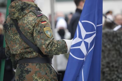 En person i militärklädsel försedd med en tysk flagga håller i en Natoflagga.