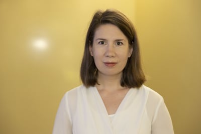 Liisa Larja seisoo aulassa. Keltainen seinä taustalla.
