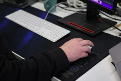 Mies pitää kättään tietokoneen hiiren päällä.