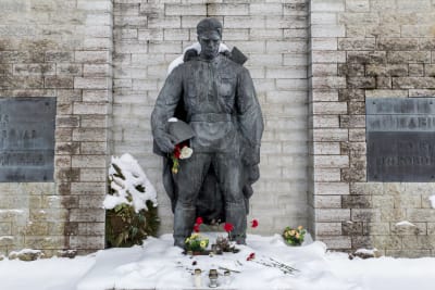 En stor staty föreställande en soldat med sin hjälm i handen. Han ser ner i marken. Kring statyn finns gravljus och blommor.