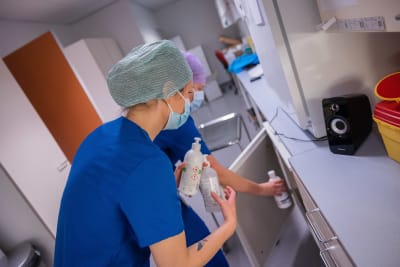 Två sjukskötare ställer in flaskor med handsprit i ett skåp. 