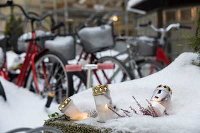 Hautakynttilöitä lumessa Ullanlinnan surmapaikan edessä 18. joulukuuta. Taustalla luminen piha ja polkupyöriä.