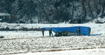 Sydkoreansk militärpolis täckte över det kraschade planet med ett plastskynke på en snötäckt risodling i Hoengseong på måndagen. 