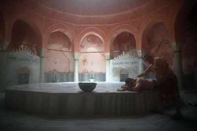 En man får massage i ett gammalt turkiskt bad. Bakom massören och mannen som masseras syns en serie valvbågar.
