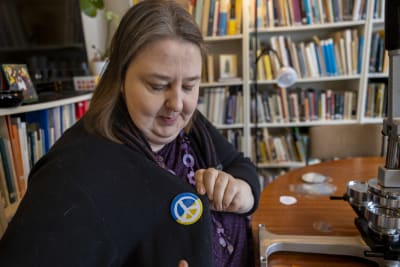 Kvinna fäster på sin tröja en pins med fredssymbol.
