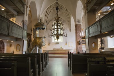 Kyrkbänkar, prediksstol och altare i en medeltida stenkyrka.