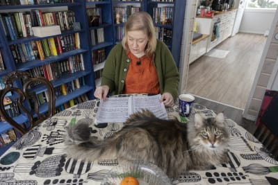 Ann-Marie Walsh sitter vid bordet och läser sin partitur. En katt sitter i förgrunden. 