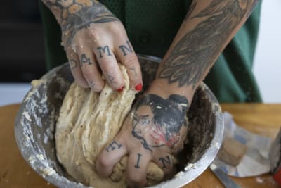 Tatuerade händer och fingrar knådar bulladeg.