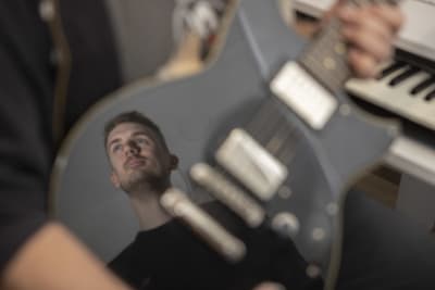 Rolf Gustavsons ansikte reflekteras från lackeringen på en gitarr,