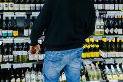 En man står framför en vinhylla med en flaska i handen.