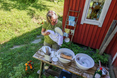 En kvinna diskar kärl på sommarstugan.