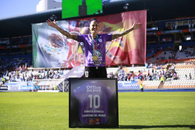 Jenni Hermoso poserar på en fotbollsplan med en medalj och inramad fotbollströja. 