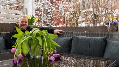 En glad man sitter bakom ett par blommor som vissnat i kylan.