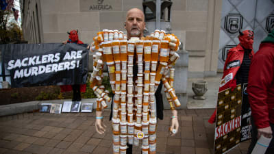 Frank Huntley, också känd som “Pill Man” står intäkt av sina egna pillerburkar i en protest mot familjen Sackler. Department of Justice building in Washington, D.C. on December 3, 2021