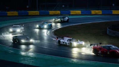 Racerbilar som kör på en regnig racerbana i mörkret.