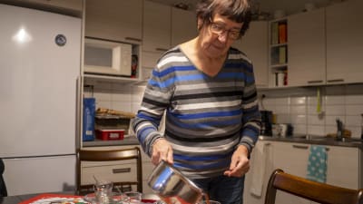 En kvinna häller i glögg från en kastrull i ryska teglas, som är finska designglas som ofta används till glögg. Hon är i ett kök.