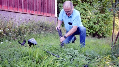 En man gräver i marken med en spade. I gräset ligger en metalldetektor.