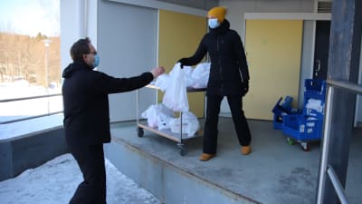 Mertalan koulun ruokapalveluesimies Päivi Raninen ojentaa etäkoululaisten ruokapakettia koulun keittiön lastauslaiturilta.