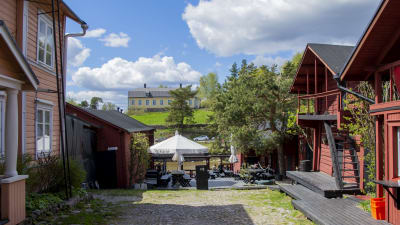 En sommarrestaurang mitt emellan två gamla hus. I bakgrunden skymtar en å och ett stort gult trähus på en kulle.
