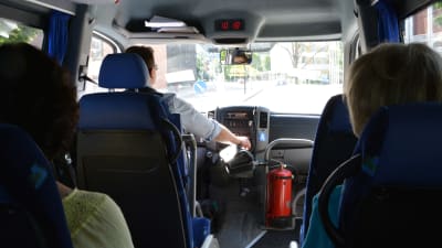 En chaufför kör en minibuss och två personer åker med.