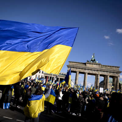 En stor ukrainsk flagga vajar över demonstranter framför Brandenburger Tor i Berlin.
